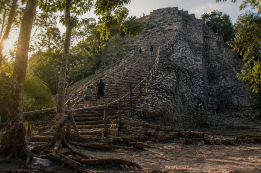A tall stone Maya pyramid rising above green jungle treetops