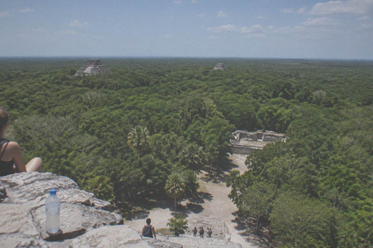 View from the summit of Nohoch Mul pyramid at Coba, looking across a vast sea of green jungle treetops under a bright sky.