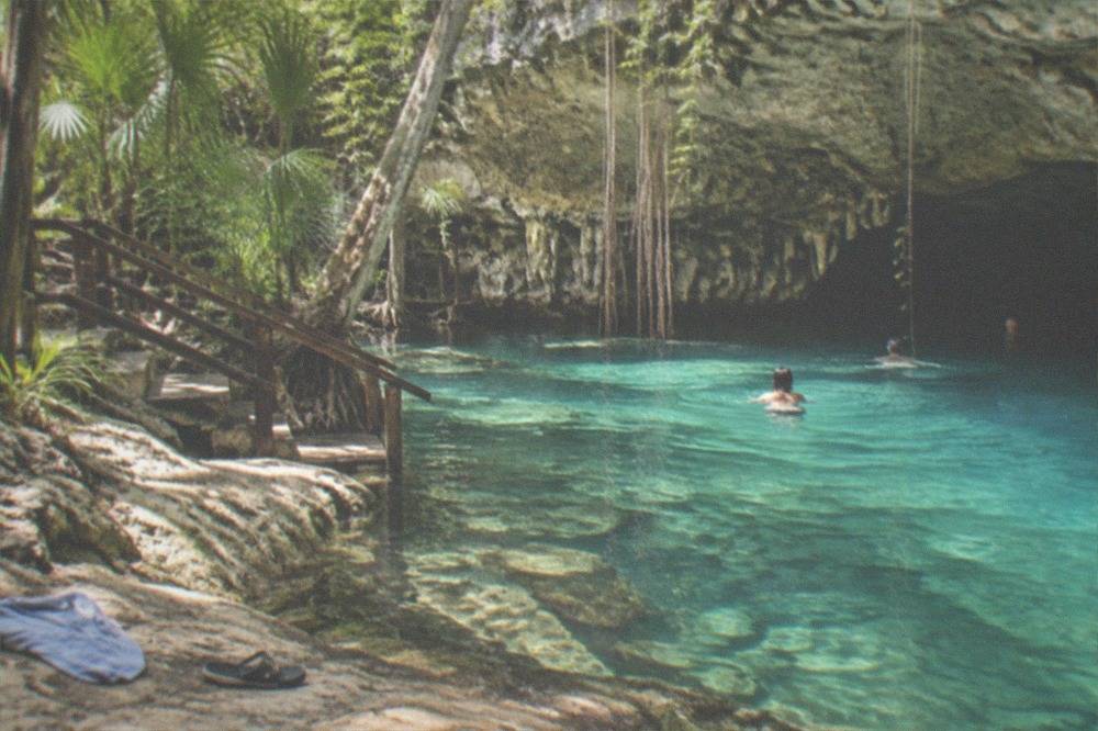 Clear turquoise water of an open cenote surrounded by limestone rock and green jungle plants