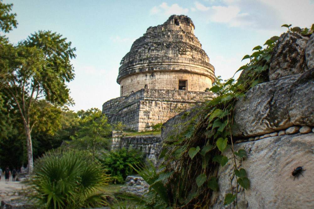 The round stone tower of the El Caracol observatory surrounded by jungle
