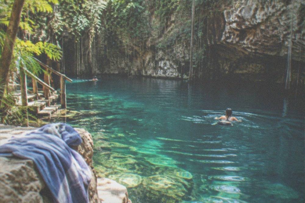 A turquoise open-air cenote ringed by rock walls and green jungle plants