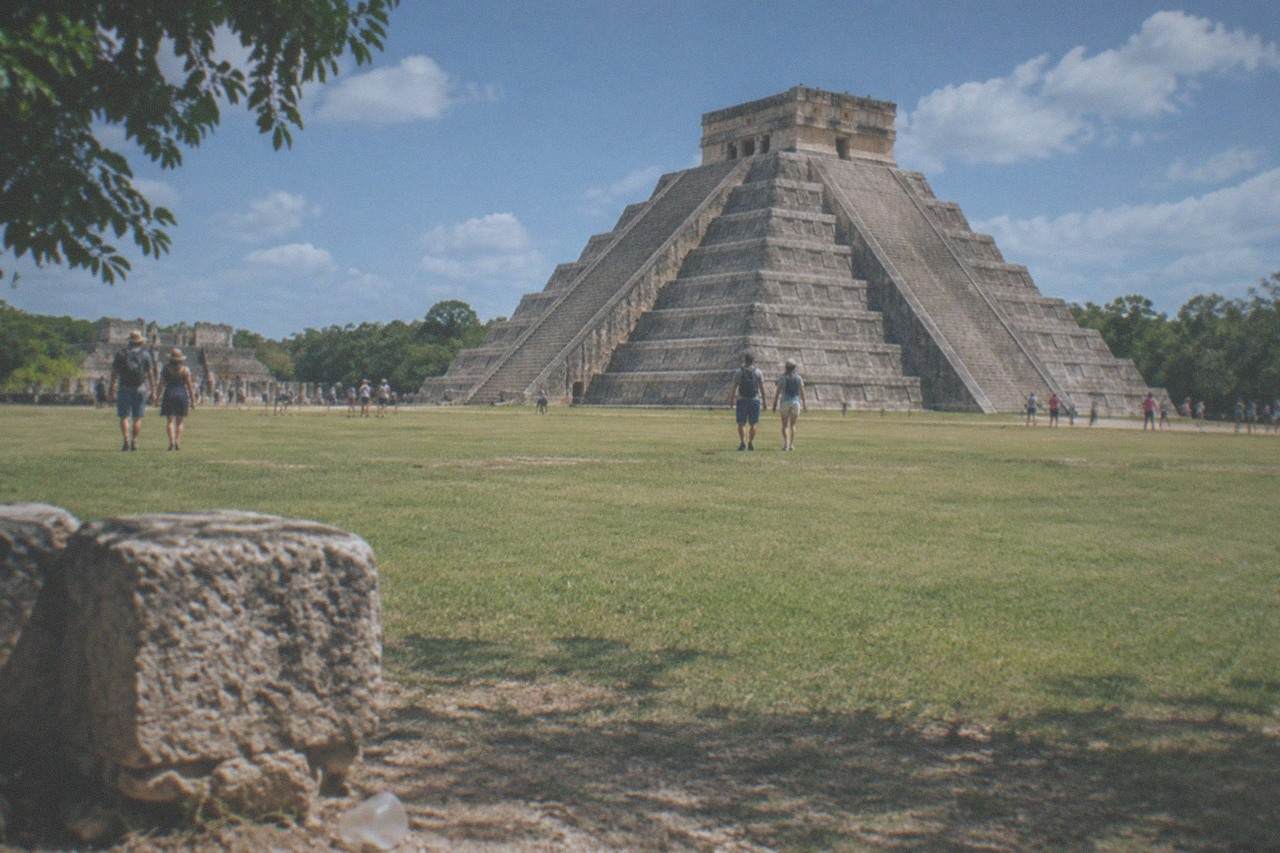 The stepped pyramid of El Castillo rising above a wide grass plaza under a bright sky