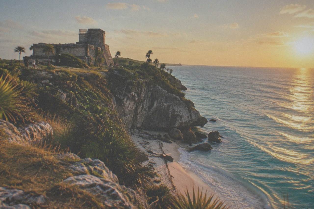 Stone ruins of a Mayan temple on a cliff above a turquoise Caribbean cove