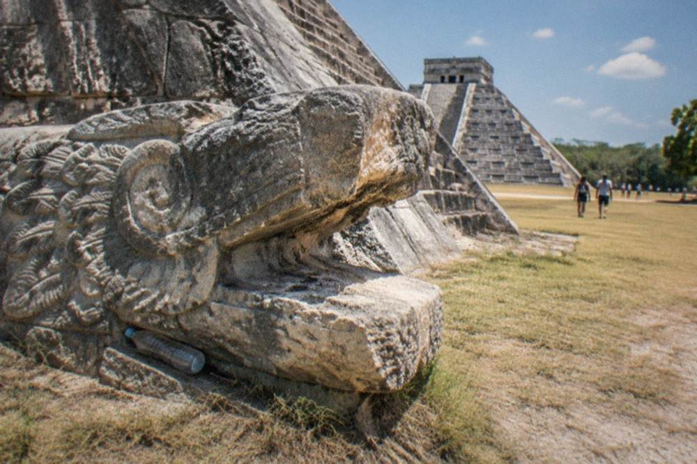Serpent head stone carving at the base of a pyramid staircase with sunlight across the stone