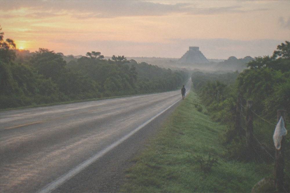 A road cutting through green jungle toward a distant pyramid on the horizon