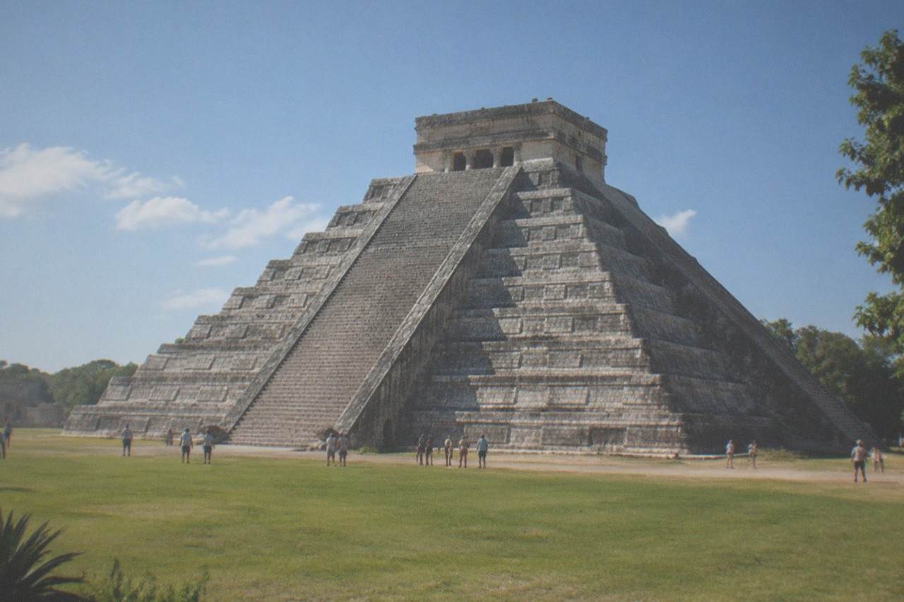The stepped stone pyramid of El Castillo at Chichen Itza under a wide sky with green lawn in front