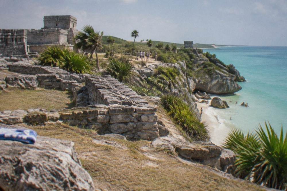 A walled Maya ruin on a cliff above a calm turquoise Caribbean cove