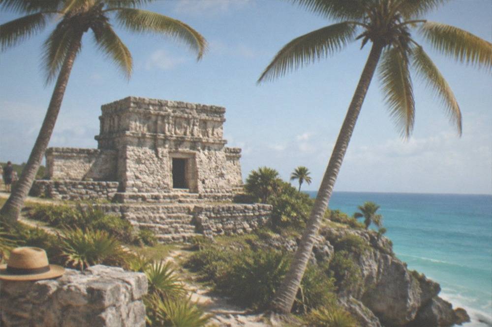 A stone Maya ruin framed by palm trees with calm sea and sky beyond