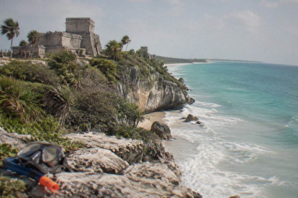 Ancient stone ruins with carved walls standing on a cliff above turquoise sea