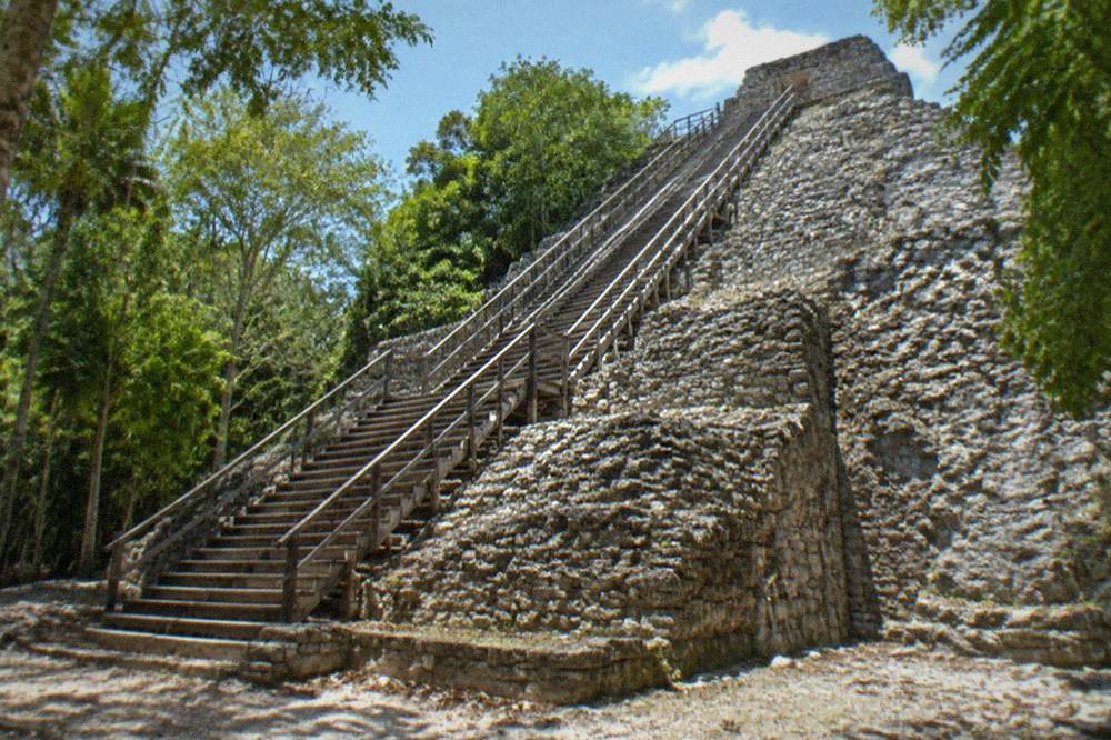 Tall stone pyramid rising above jungle trees with a wooden staircase on one face