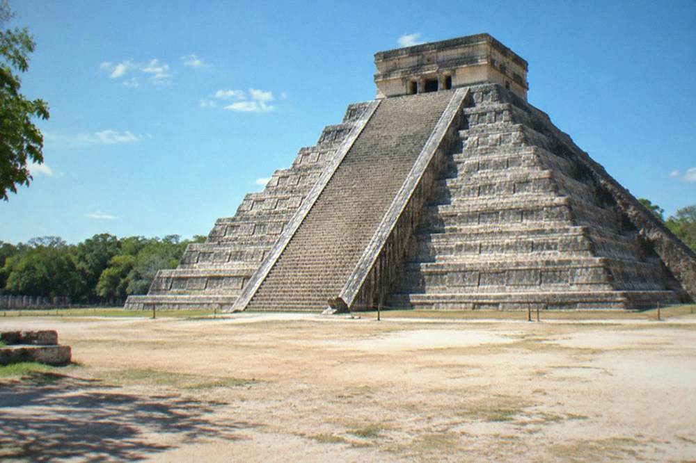 A tall stone pyramid rising above dense jungle canopy under a clear sky