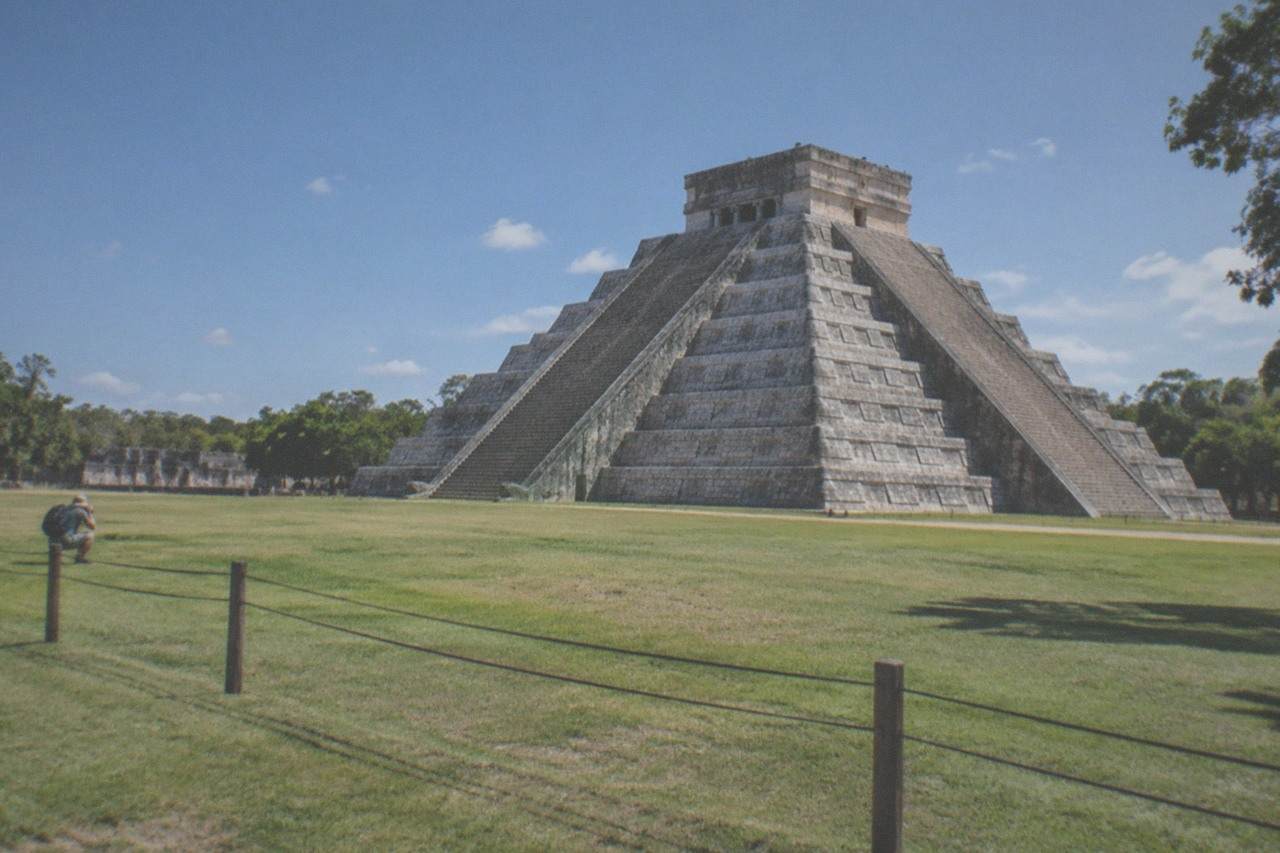 El Castillo pyramid at Chichen Itza seen from the grass plaza under a blue sky