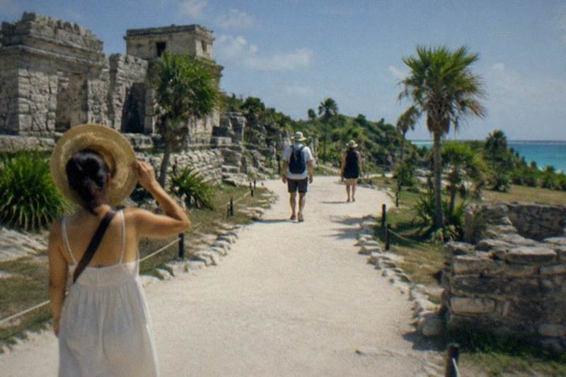 Visitors walking the stone paths of the Tulum archaeological zone among clifftop Maya ruins