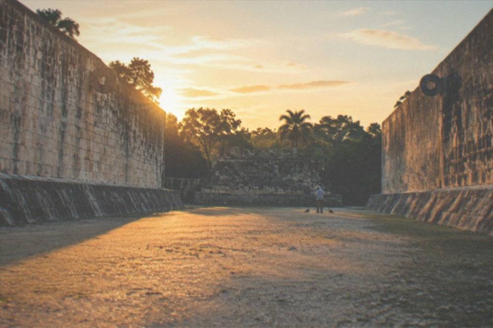 A wide stone plaza with columned ruins and visitors walking a packed earth path in morning light