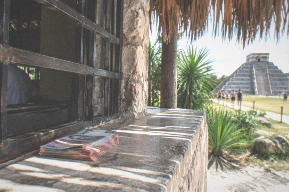 A ticket window with a hand passing over peso bills under a thatched palapa roof
