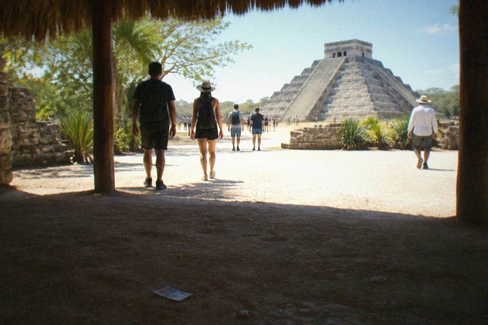 A shaded ticket entrance walkway at an archaeological park with visitors queueing