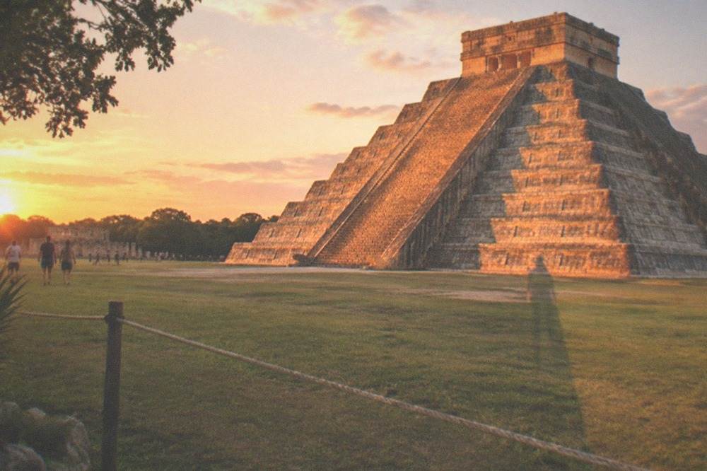 A tall stepped stone pyramid seen from behind a low rope barrier on mown grass