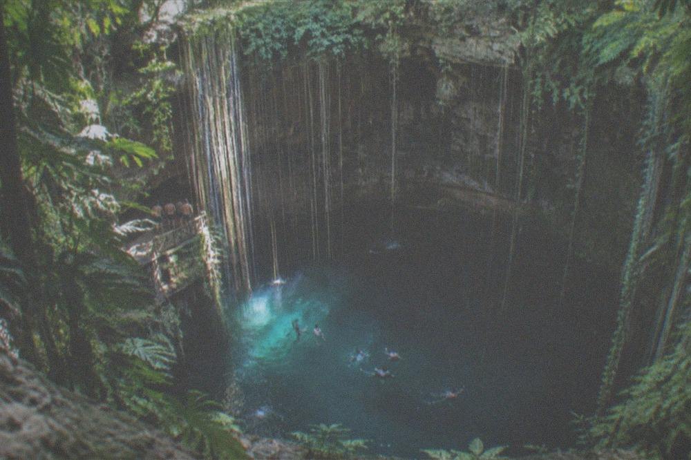 A turquoise open-air cenote surrounded by rock walls with a wooden entry platform