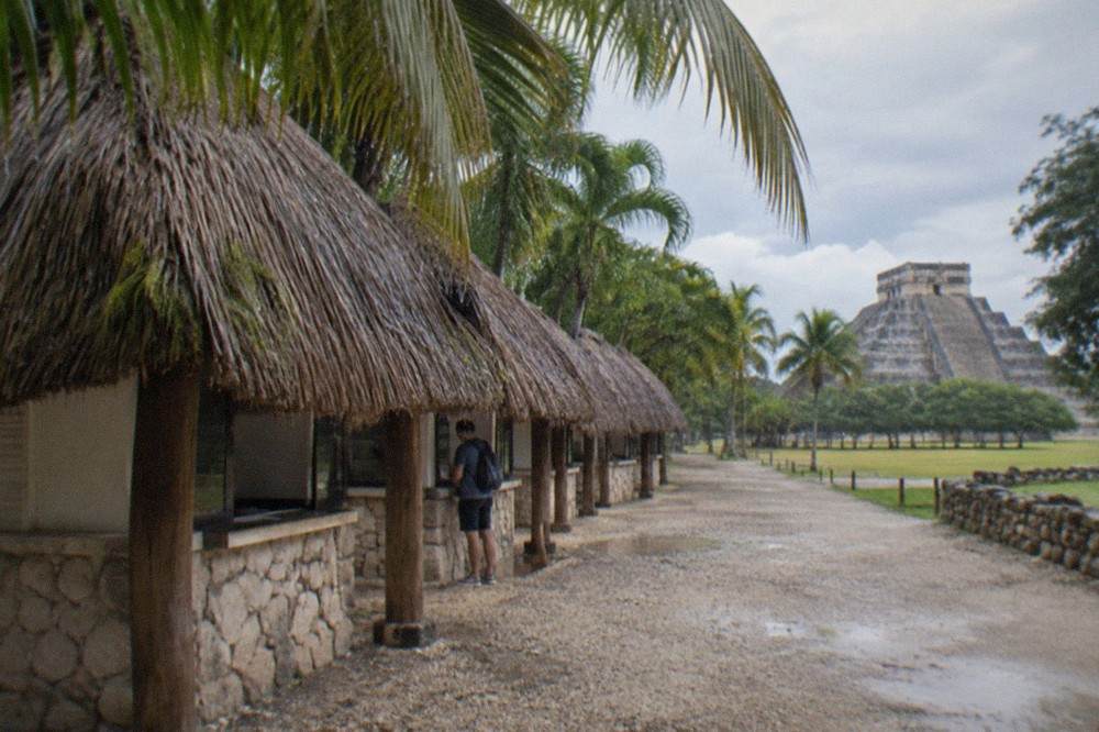 A stone ticket window with a thatched palapa roof at the entrance to the Chichen Itza archaeological site