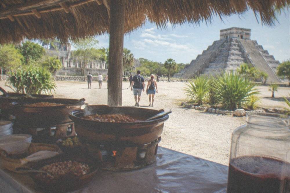 A regional buffet lunch laid out on a table under a thatched roof near the Chichen Itza site