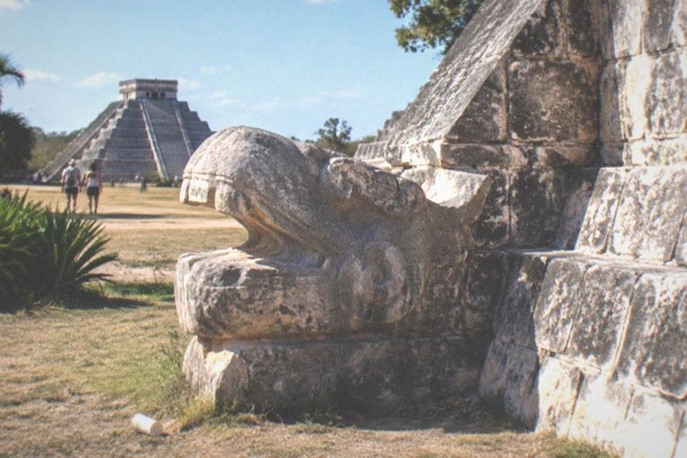 A carved stone serpent column at a restored temple base at Chichen Itza in late morning light