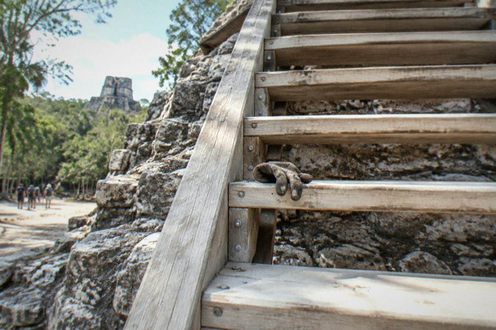 Tall stone pyramid with a wooden staircase rising over jungle treetops
