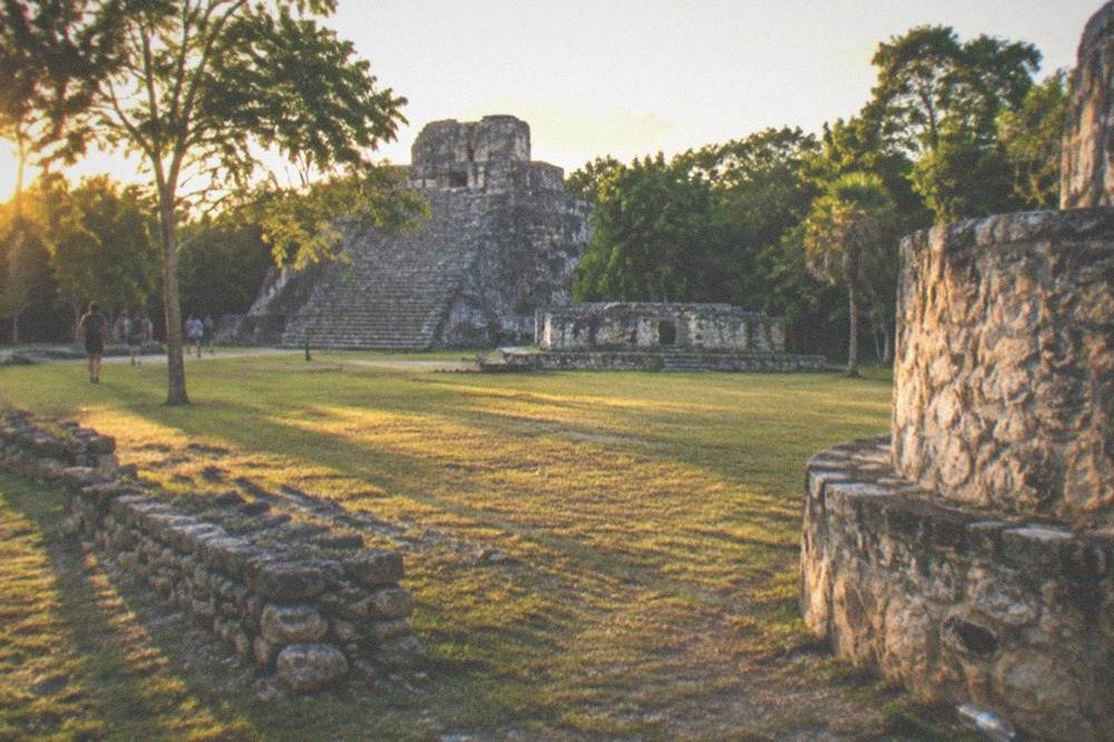 Wide view of a restored stone ruin group surrounded by green jungle at Coba