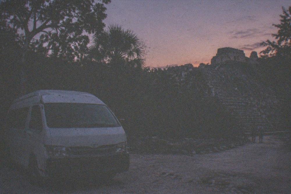 Small tour van parked on a gravel road beside jungle at the edge of the ruins