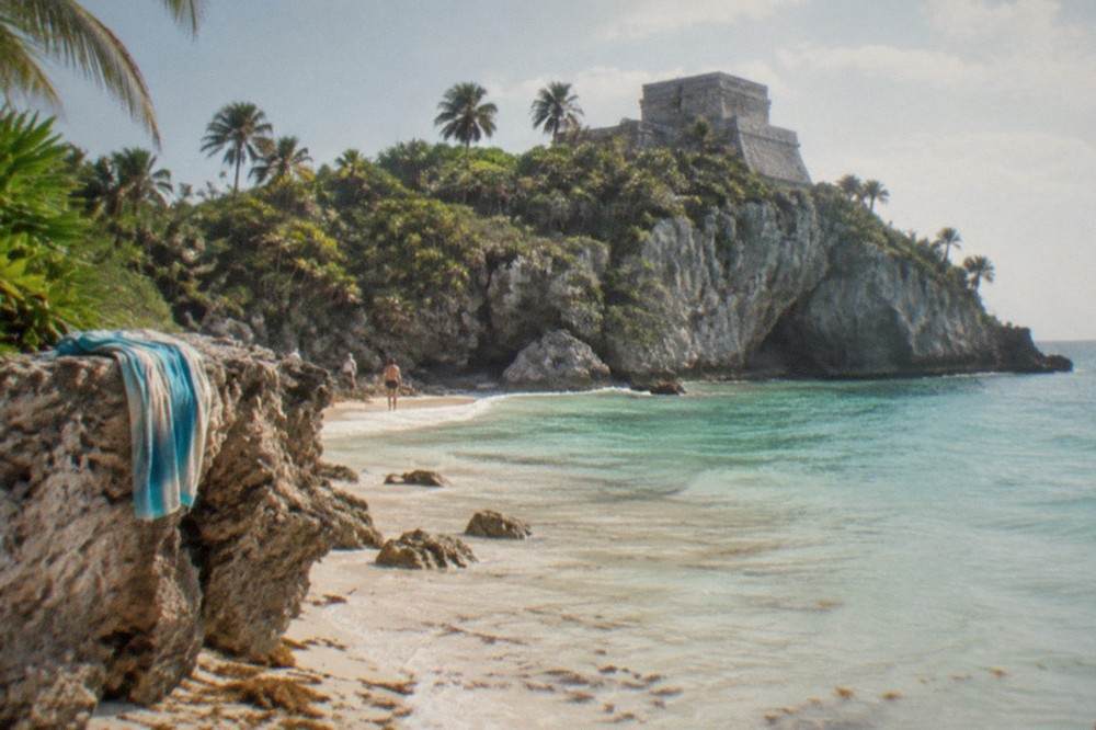 Small sandy cove with calm turquoise water below stone cliffs at the Tulum ruins