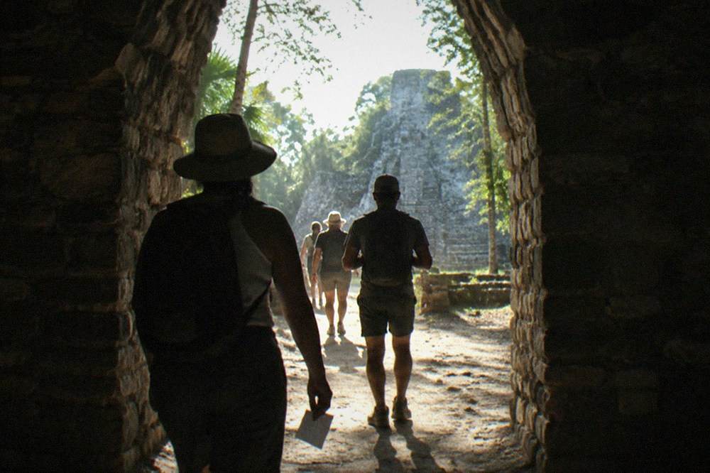 A stone archway entrance to a Mayan archaeological site with visitors walking through