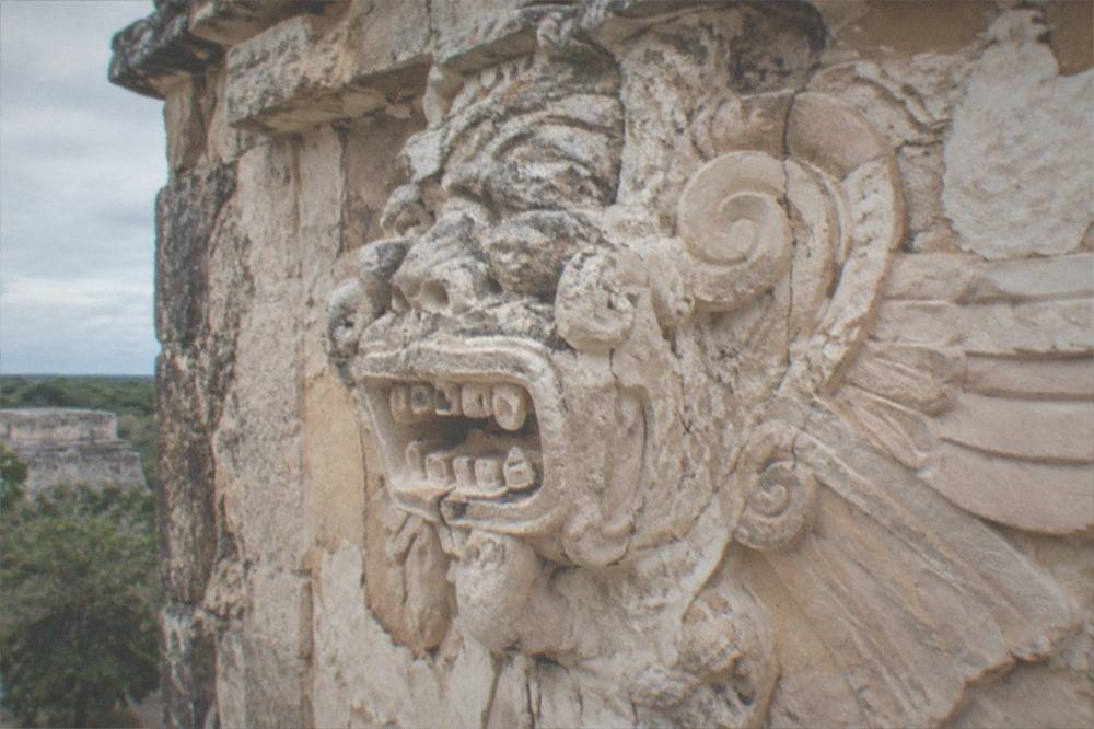 Carved stucco figures on the facade of a Mayan acropolis structure under open sky