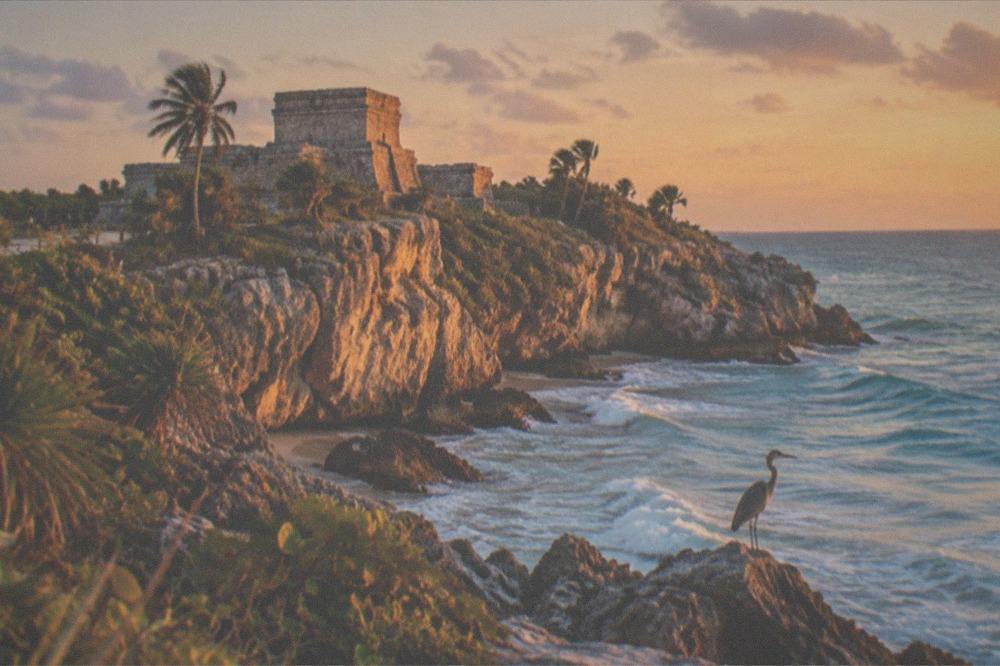 A Mayan stone temple overlooking turquoise Caribbean water from a cliff