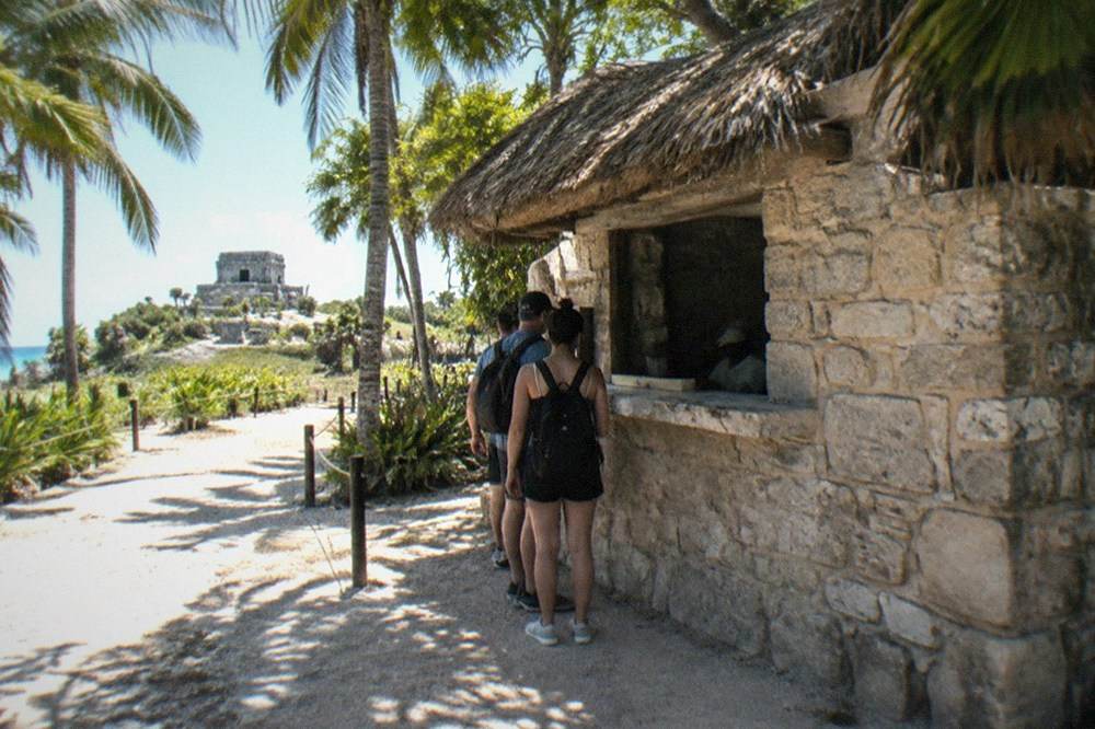 A stone ticket booth and entrance path at a Mayan archaeological site surrounded by trees