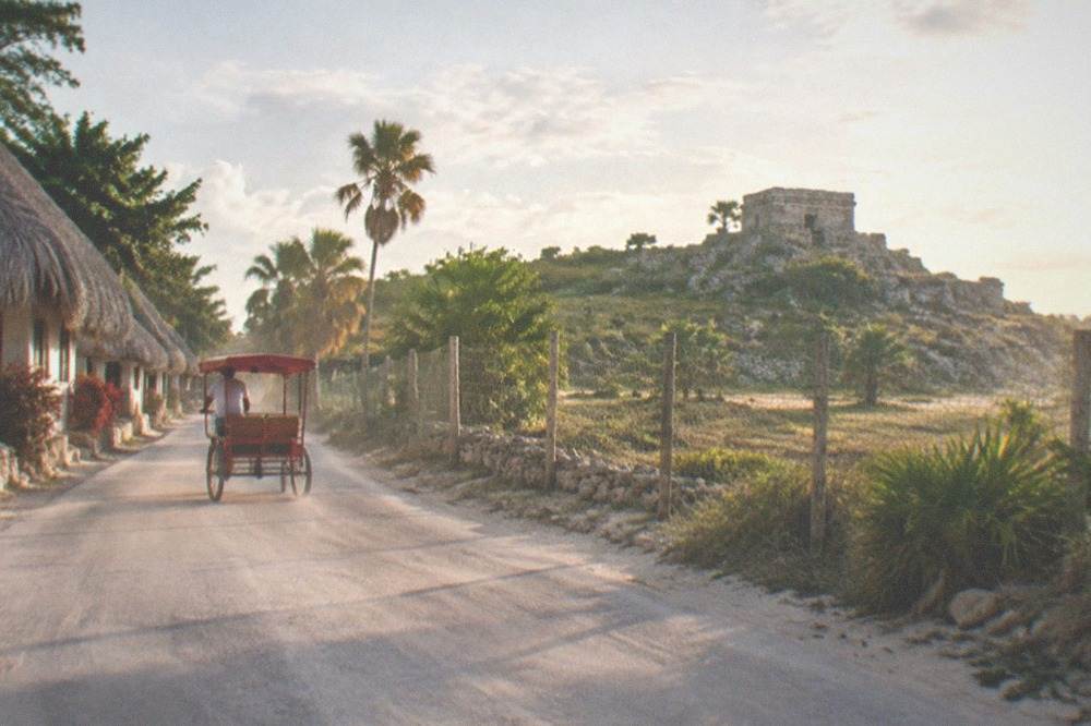 A paved road through tropical jungle with a small stone ruin visible in the distance