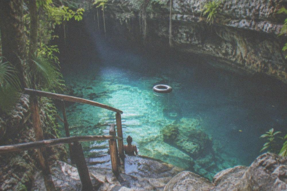 A turquoise cenote surrounded by rock and jungle with sunlit clear water