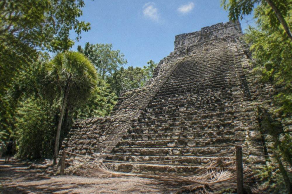A stepped stone pyramid rising above dense green jungle under a blue sky