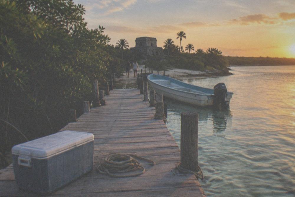 A wooden dock extending into clear shallow lagoon water with mangroves along the shore