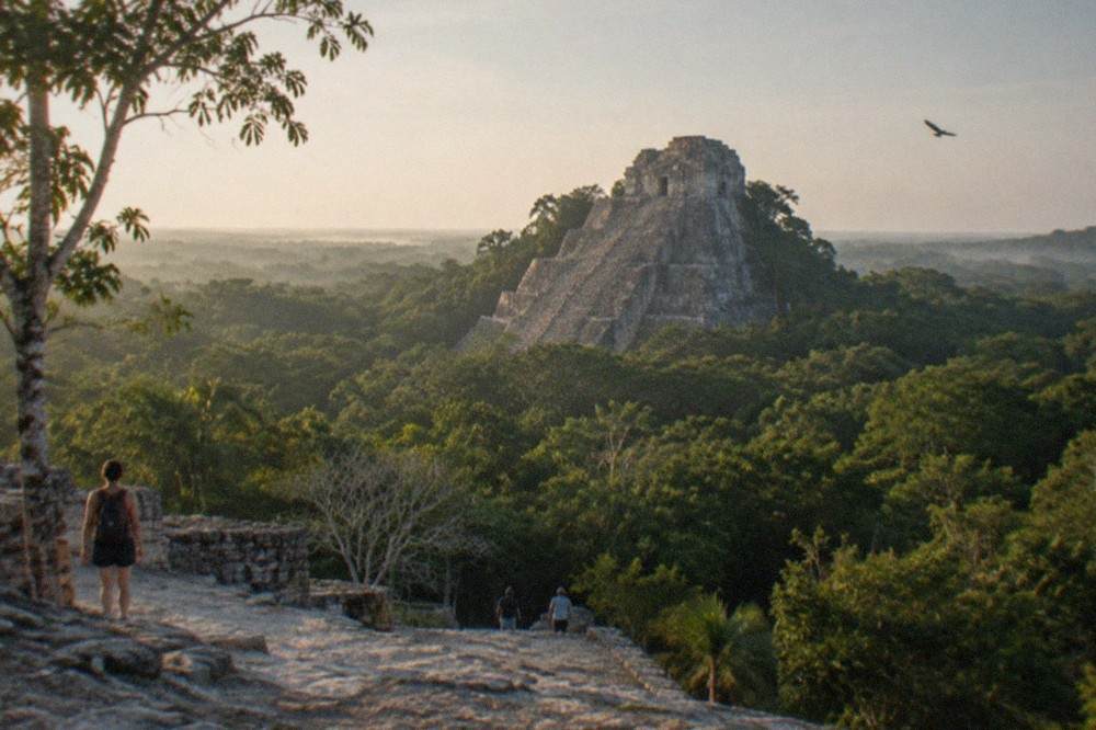 A tall stone Maya pyramid rising above dense green jungle canopy