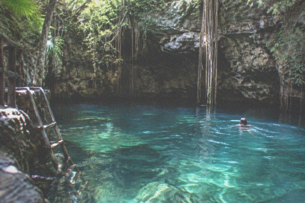A shallow turquoise cenote surrounded by rock walls and jungle vegetation