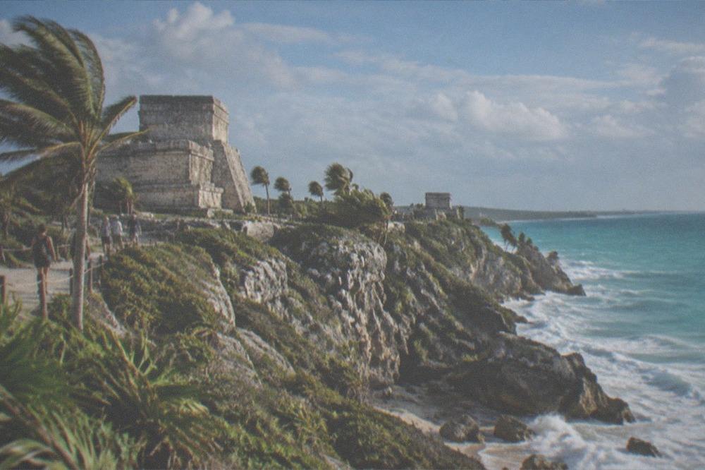 A stone Maya fortress wall overlooking turquoise Caribbean water from a cliff
