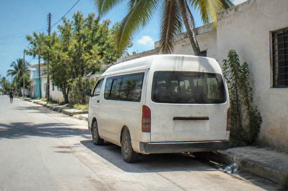 A white colectivo van parked on a sunny street in Tulum town