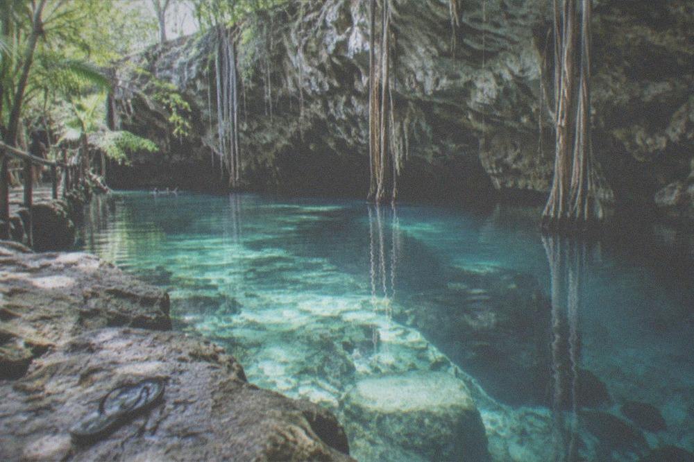 Clear turquoise water in an open jungle cenote surrounded by rock and greenery