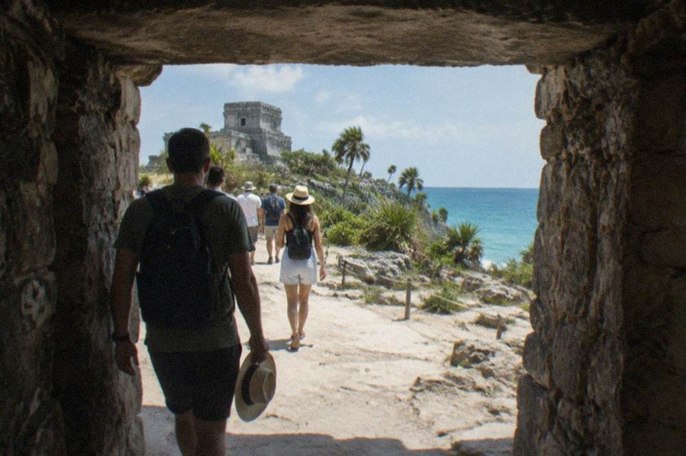 A stone gateway in the Tulum ruins wall with visitors walking the path in morning light