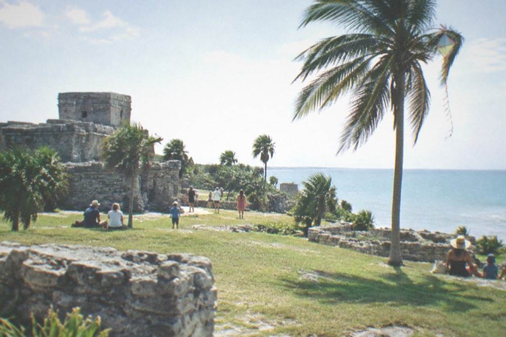 Visitors gathered on the grass inside the walled Tulum archaeological zone on a bright day