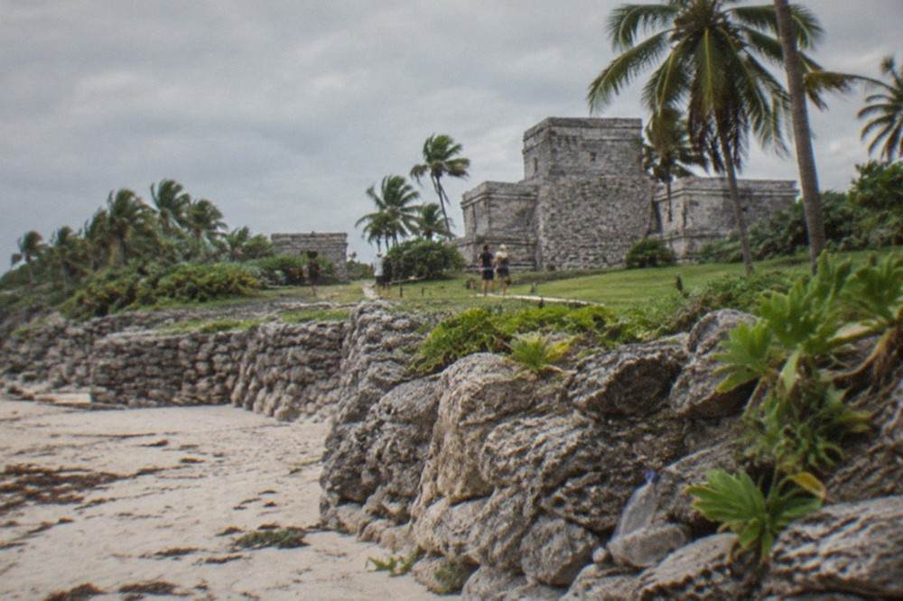 Low stone walls of a Maya fortification enclosing a grassy site near the sea
