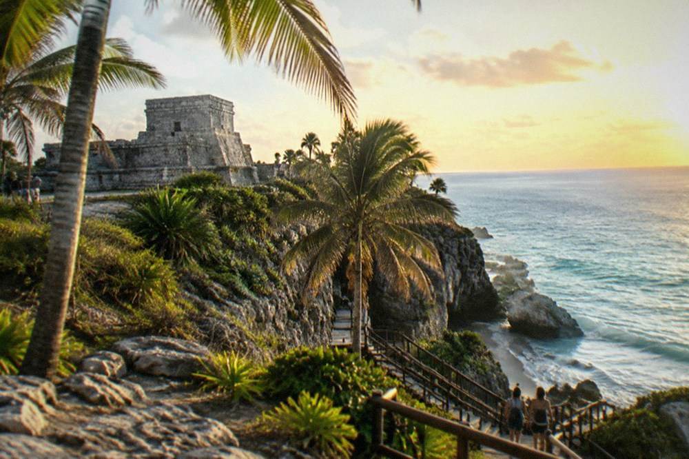 A stone temple platform overlooking palm trees and open Caribbean water