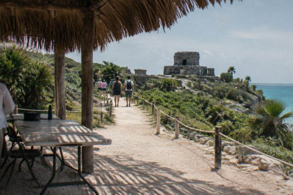 Ticket entrance area of the Tulum archaeological zone with a thatched shade structure and stone path