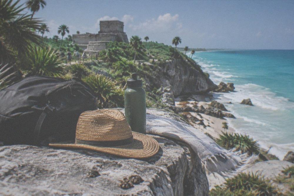A visitor's backpack, hat and water bottle on a stone ledge overlooking the Caribbean