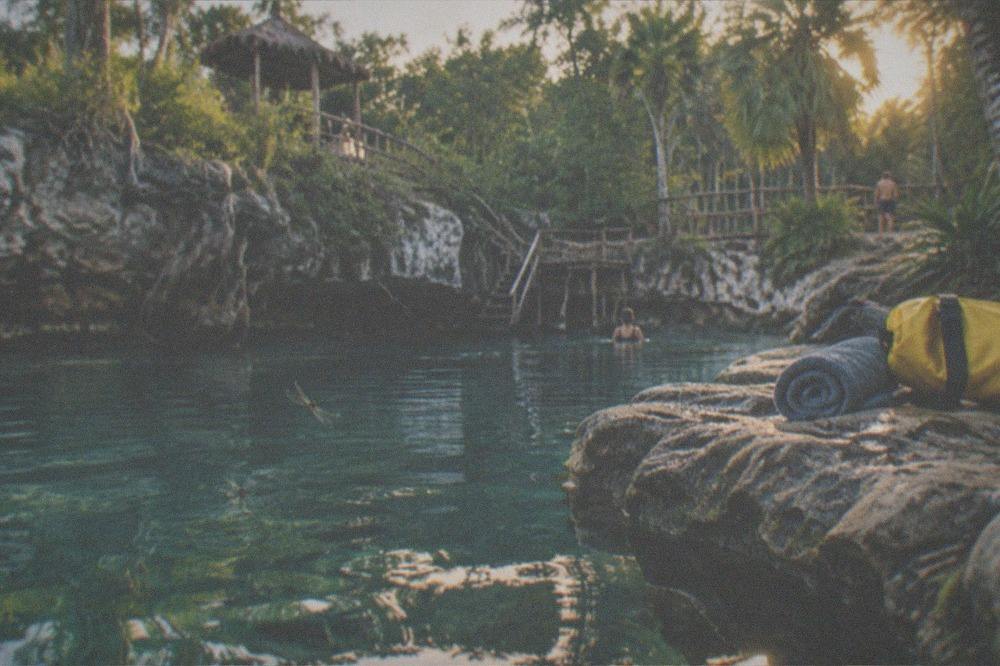 A dry bag and towel set out beside a sunlit jungle cenote near Tulum